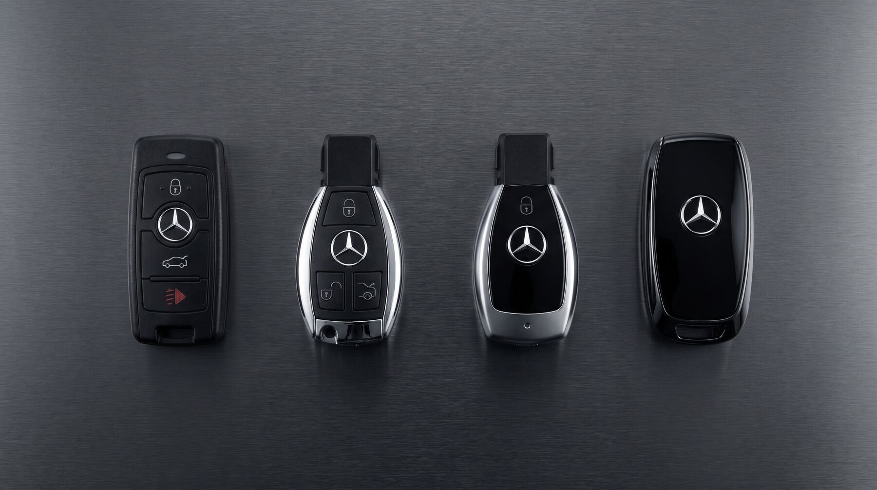 Четыре ключа Mercedes-Benz разных поколений на тёмной металлической поверхности